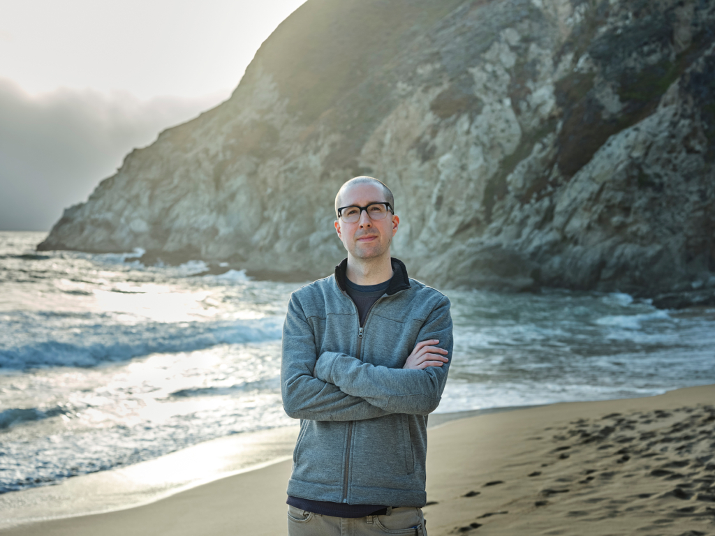 persons standing on a beach with the ocean behind him